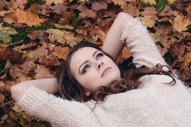Mujer tumbada sobre hojas secas en un parque recordando el pasado