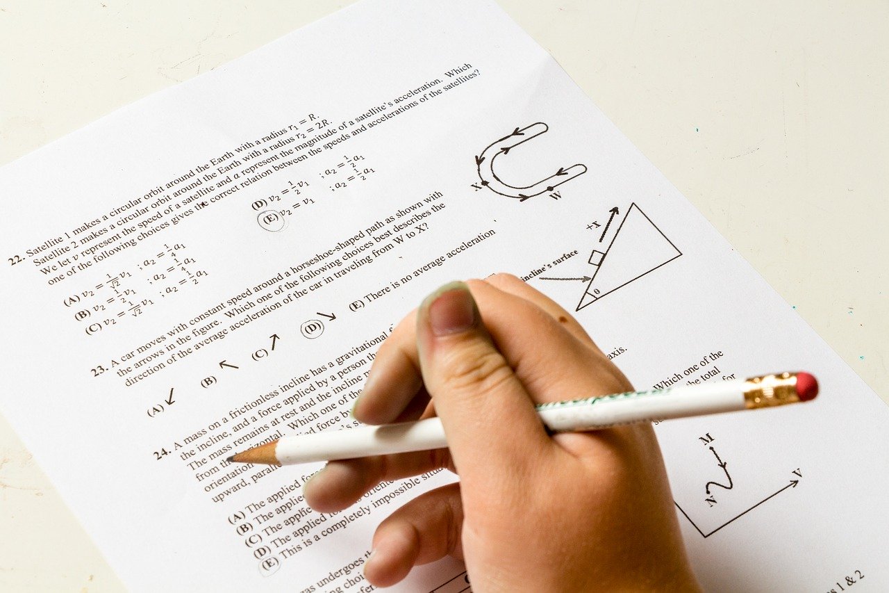 Imagen de una hoja de examen de matemáticas y una mano con un lápiz como resolviéndolo